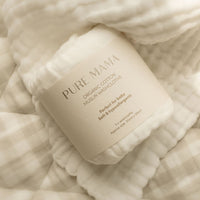 A rolled-up pack of Pure Mama NZ Organic Muslin Set washcloths rests on an ivory checkered blanket, featuring the eco-friendly label Perfect for baby, soft & hypoallergenic. The washcloth boasts a gentle, textured surface.