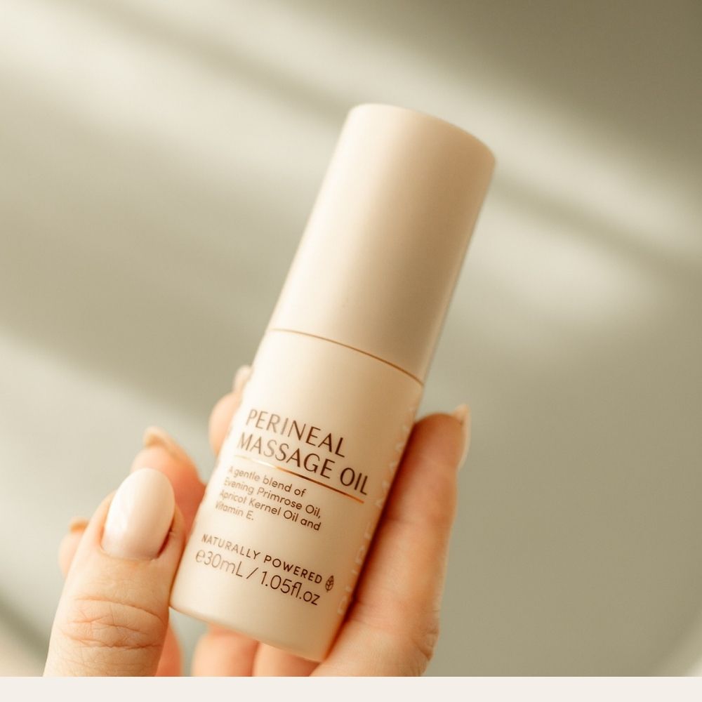 A hand with neatly manicured nails holds a 30 mL beige bottle of Pure Mama NZ Perineal Massage Oil, formulated to support birth recovery and help minimize perineal tearing, set against a softly blurred background.