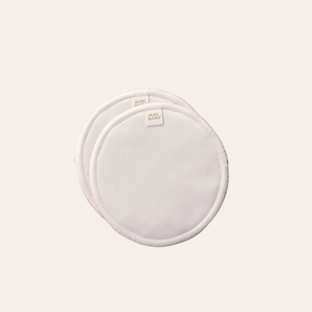 Two overlapping, round, white PURE MAMA Skincare Nursing Pads (set), made of reusable bamboo with stitched edges and small fabric tags, placed on a plain light background.