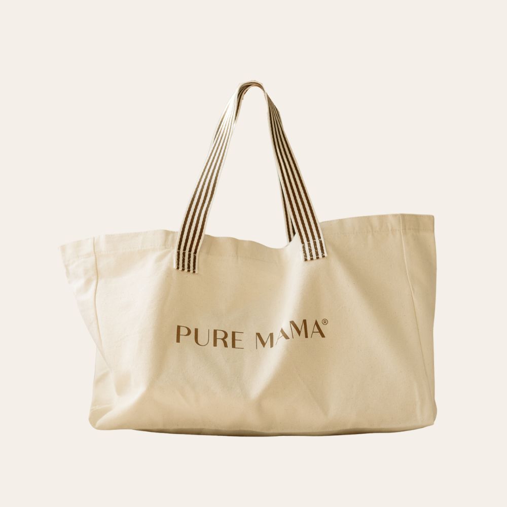 The Luxe Large Tote Bag by PURE MAMA Skincare in beige features PURE MAMA in brown on the front and black-and-white striped handles, shown against a plain, light background.