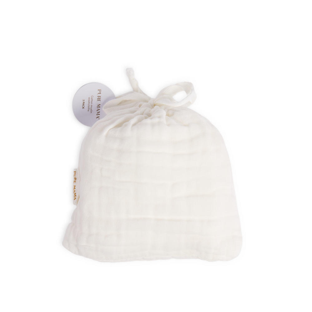 An off-white muslin baby swaddle blanket, gathered inside a matching drawstring bag with a small brand tag and a circular product tag attached, set against a plain white background.