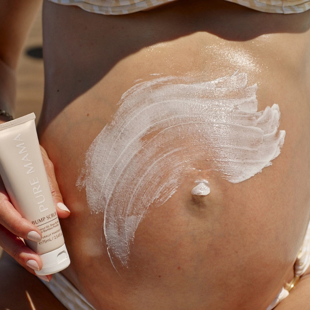 A person applies a generous amount of white cream from a Pure Mama NZ Belly Spa Kit tube to their bare, pregnant belly, enjoying a luxurious self-care moment.
