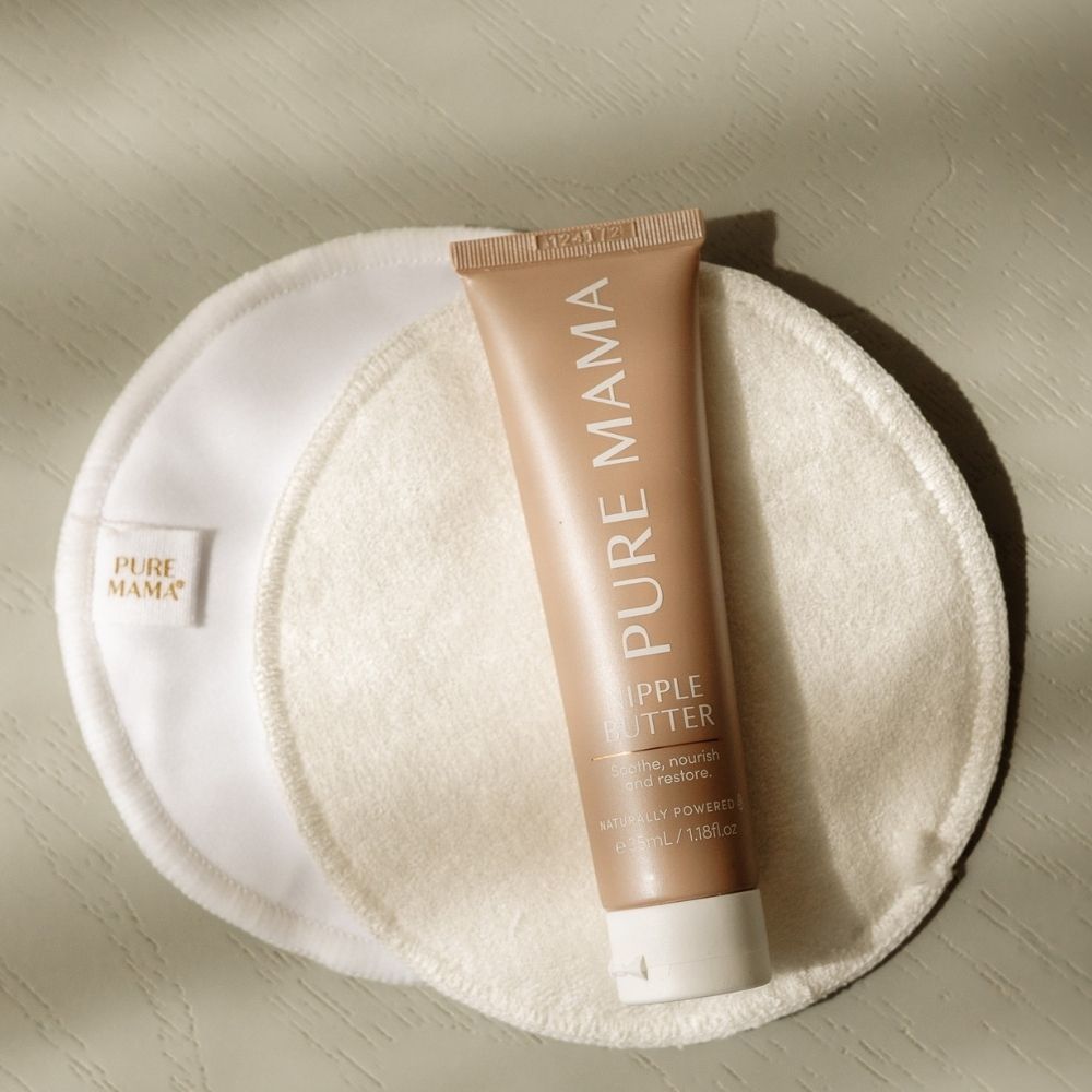 A tube of Pure Mama NZ Nipple Butter sits on two white reusable pads atop a light, textured surface. This organic balm soothes and restores skin—ideal for nourishing breastfeeding mothers.