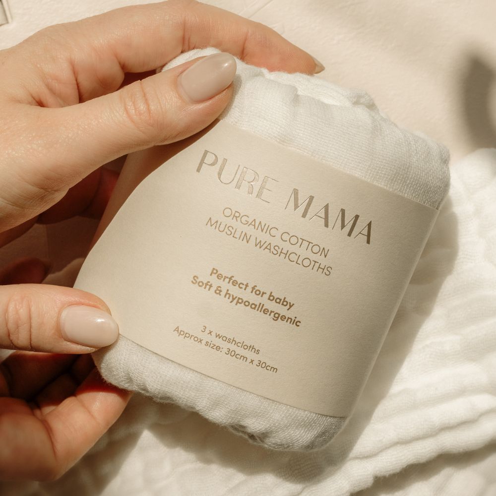A close-up shows a hand holding a white pack of Pure Mama NZ Organic Muslin Set, labeled Perfect for baby, Soft & hypoallergenic, with beige-painted nails.