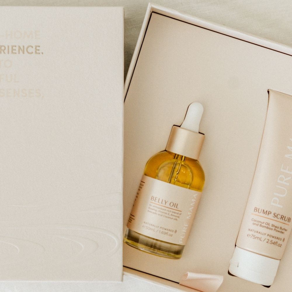 A beige gift box from Pure Mama NZ contains the Belly Spa Kit with a dropper bottle of Belly Oil and a tube of Bump Scrub, both in minimalist, natural-toned packaging—perfect for soothing pregnancy self-care.